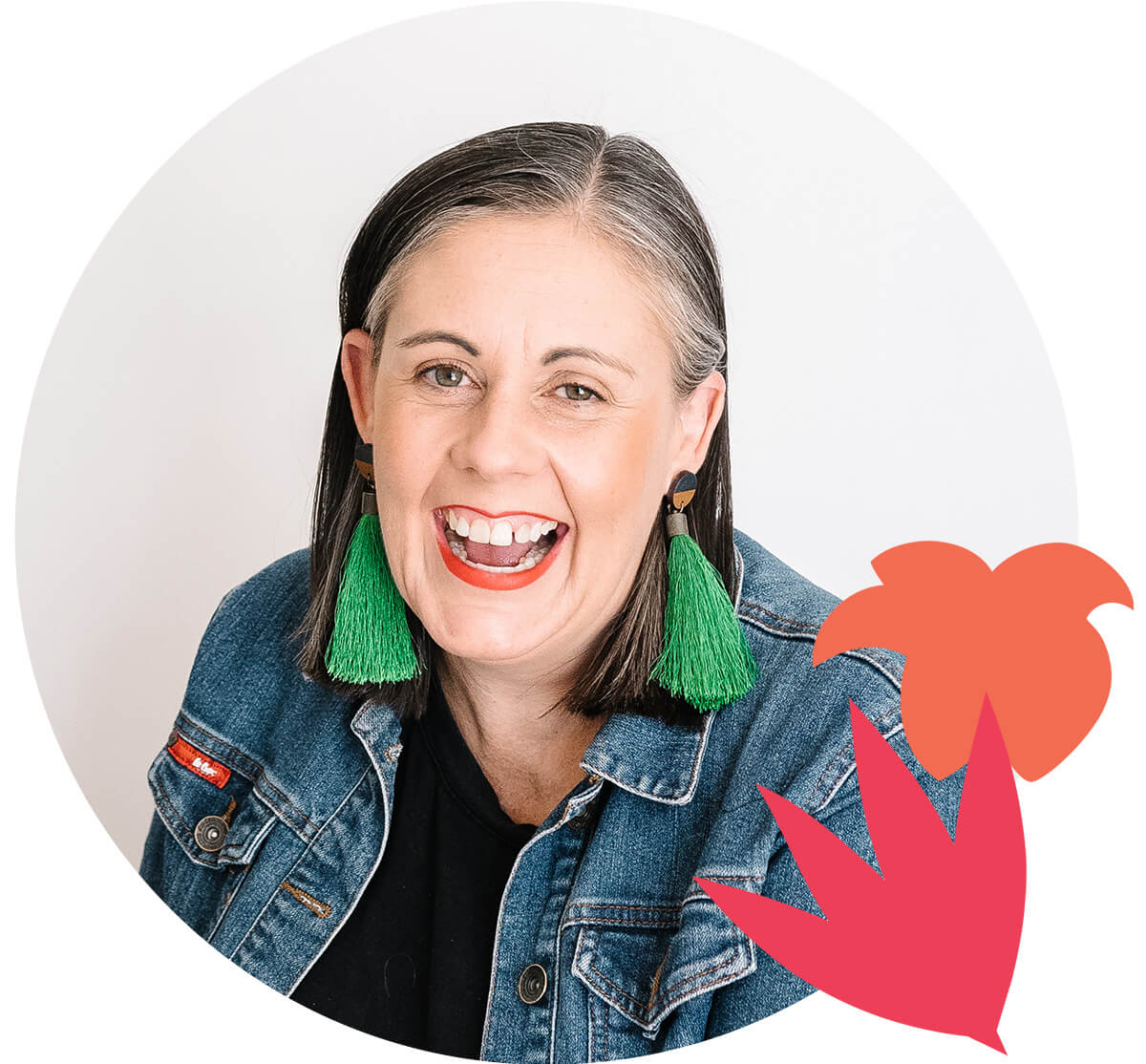 A woman with dark, grey streaked hair and long green earrings. She's wearing a denim jacket. She is Angela Pickett Sales page copywriter